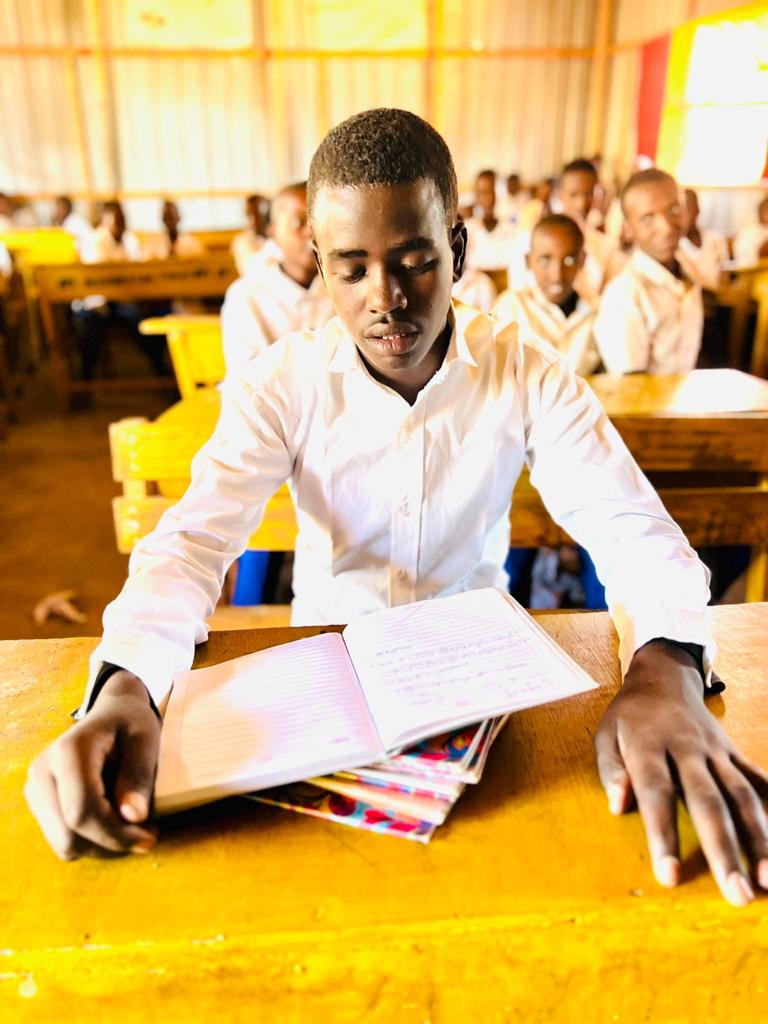 A teenager sits at a school desk in a classroom reading a textbook