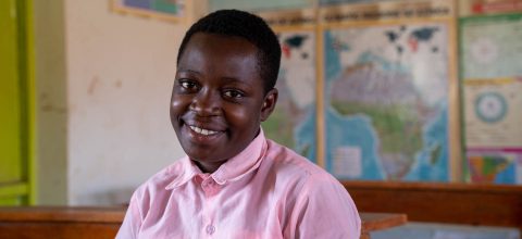 A Ugandan girl sitting at a desk in a classroom.