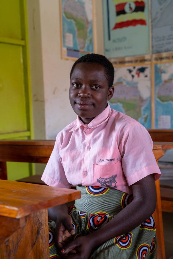 A Ugandan girl sitting at a desk in a classroom.
