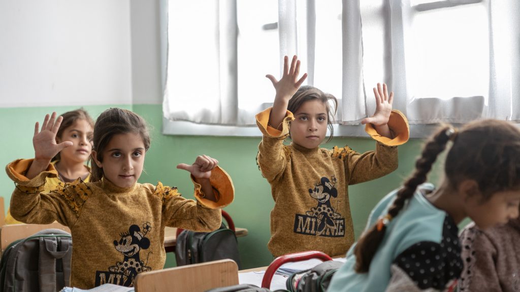 Schoolchildren hold up their hands to show different numbers of fingers in a classroom