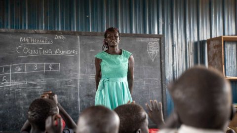 A woman stands in front of a black board in Kenya.