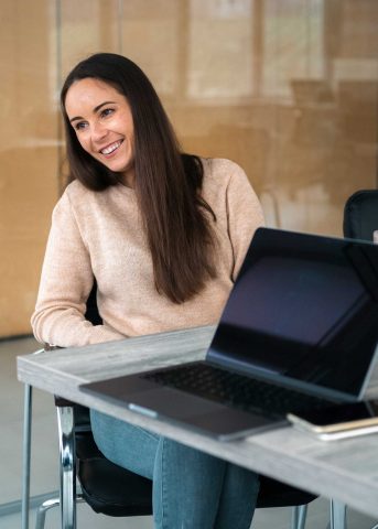 A Ukrainian woman sits by a desk. There is a laptop on the desk.