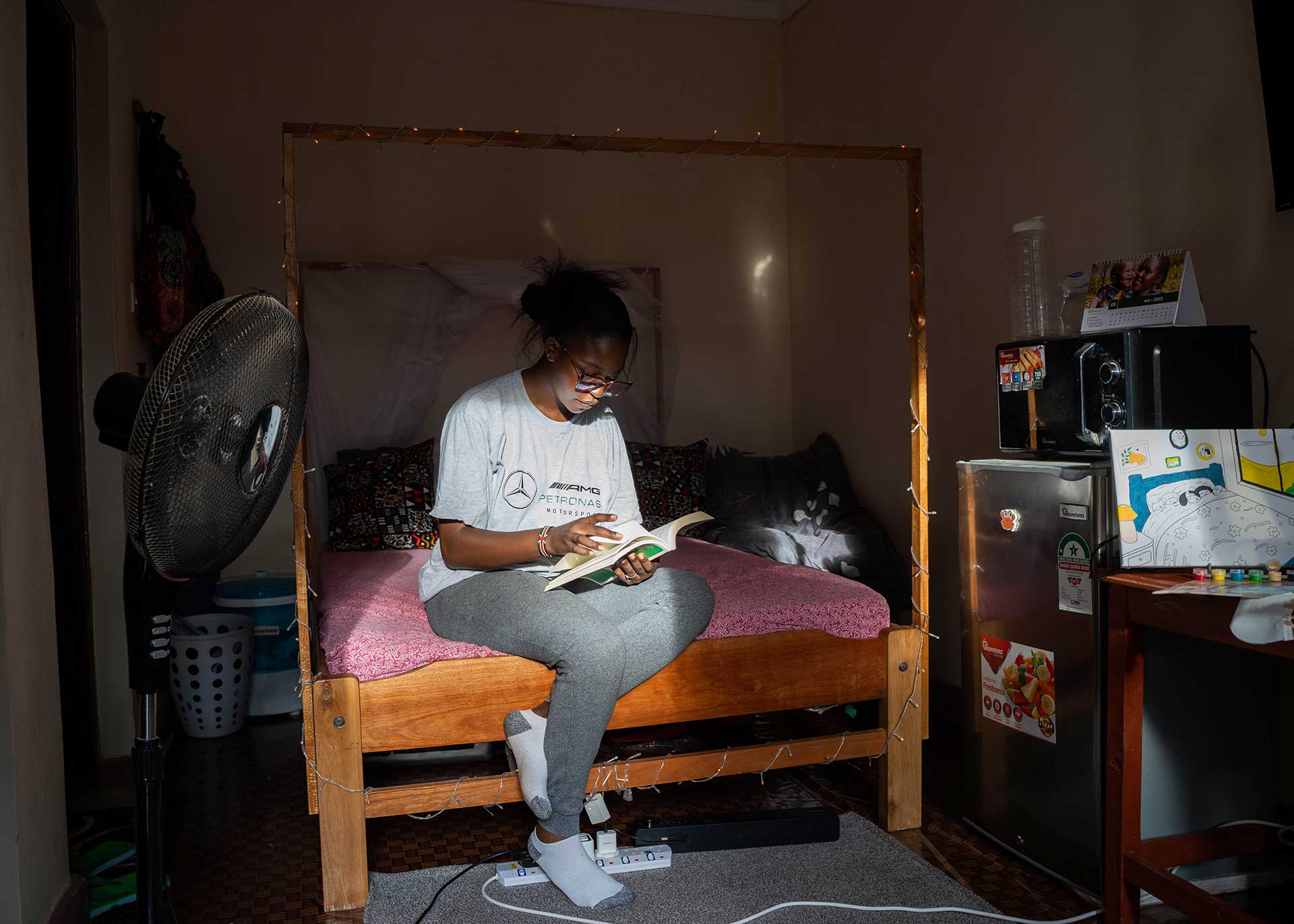 A woman sits on a bed reading in a dark room in Kenya.