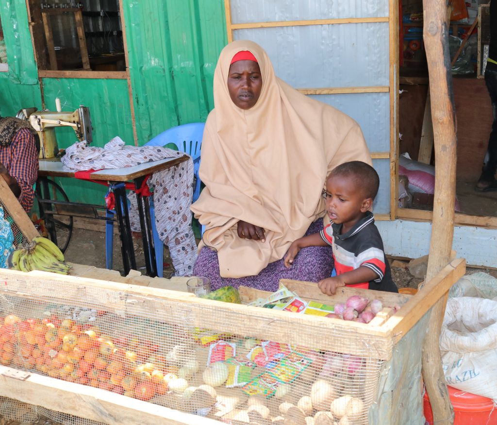 A woman and a child sit behind a stall full of vegetables