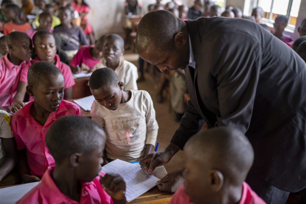 A teacher in a classroom bends over the desk of a pupil in a classroom to check some work