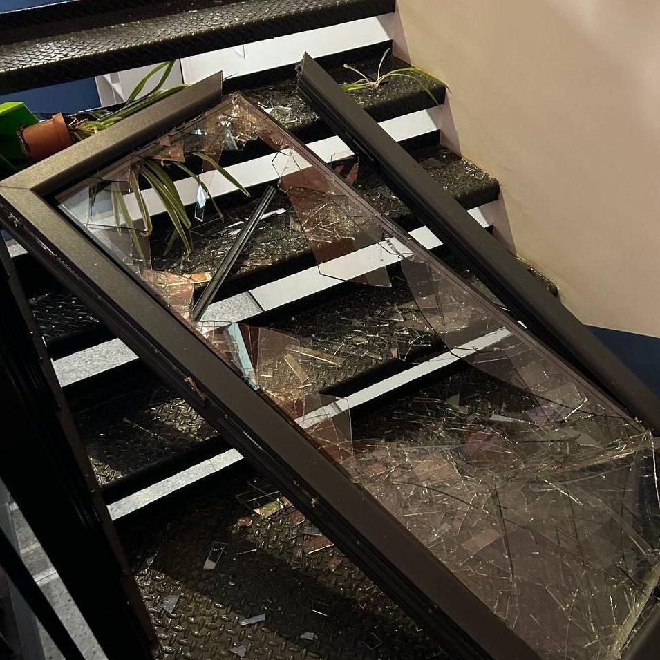A broken window lies on a staircase on top of a toppled pot plant.
