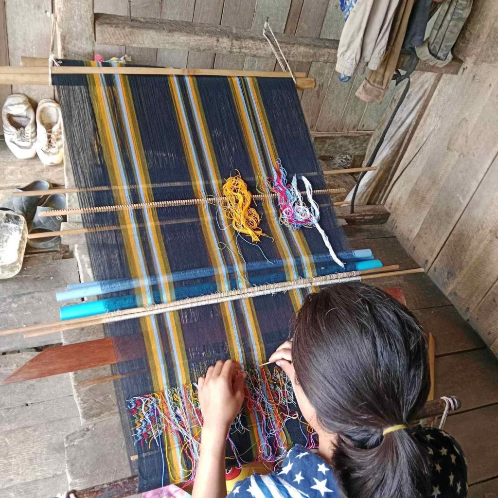 A woman hunches over a weaving frame, busily working