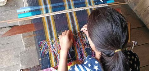 A woman hunches over a weaving frame, busily working