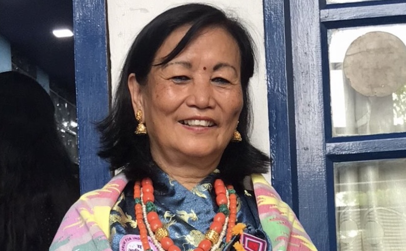 A smiling woman wearing a patterned jacket and colorful beads looks at the camera. She has a red bindi on her forehead.