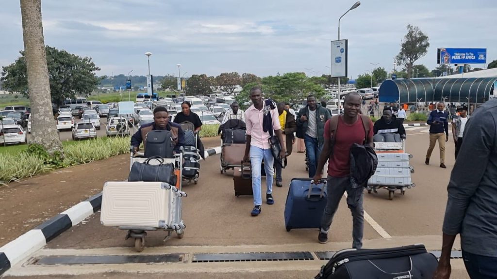 A group of young people push trolleys full of luggage on the pathway towards an airport