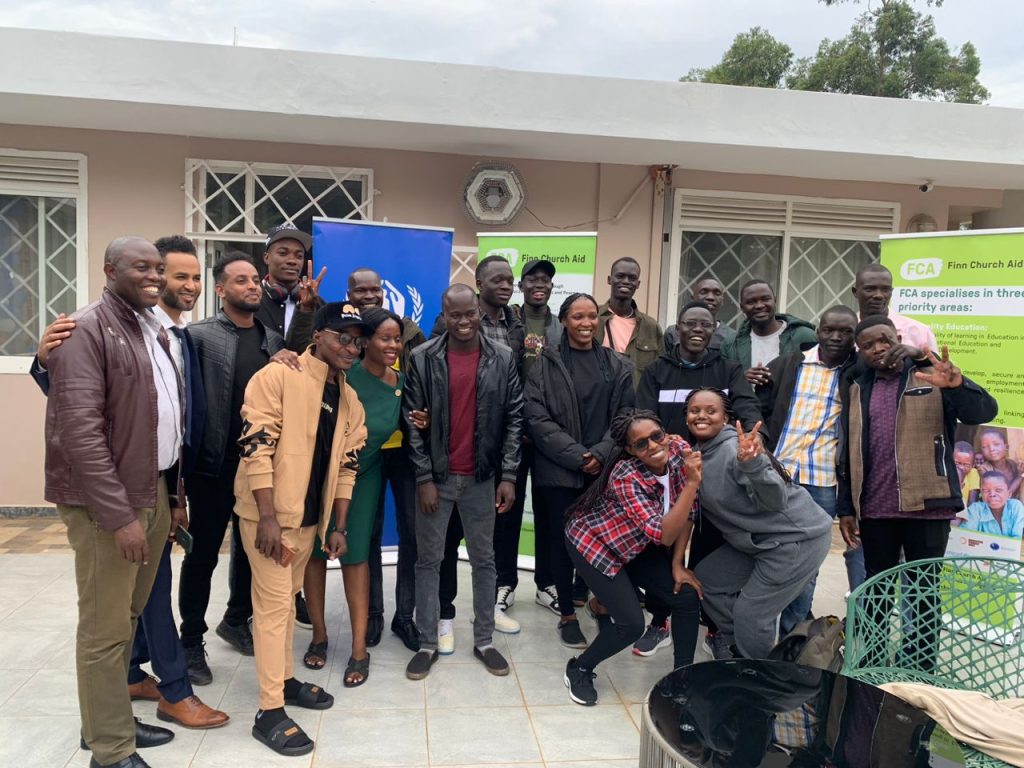 A group of young people pose for a photo outside of FCA's offices in Uganda. They are laughing and one woman at the front is showing peace signs with her fingers