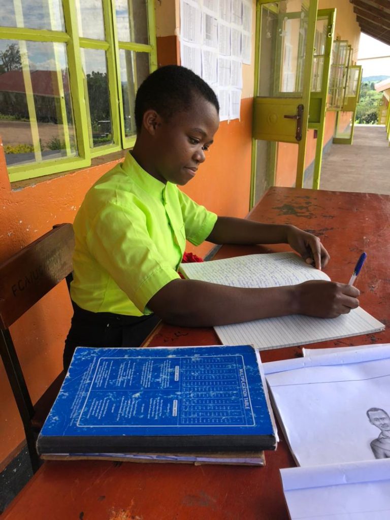 A girl in a green polo shirt sits at a desk and works on some schoolwork