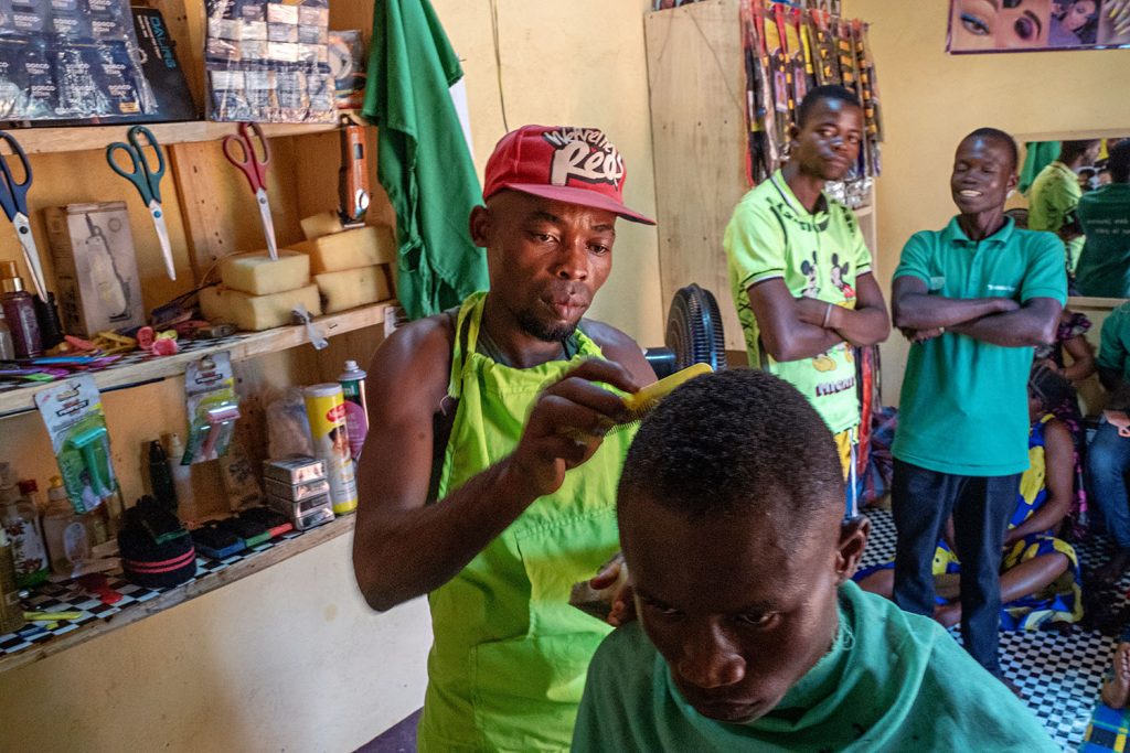 En kepsbärande man kammar en annan mans hår i Centralafrikanska republiken. I bakgrunden tittar två andra män på arbetet.