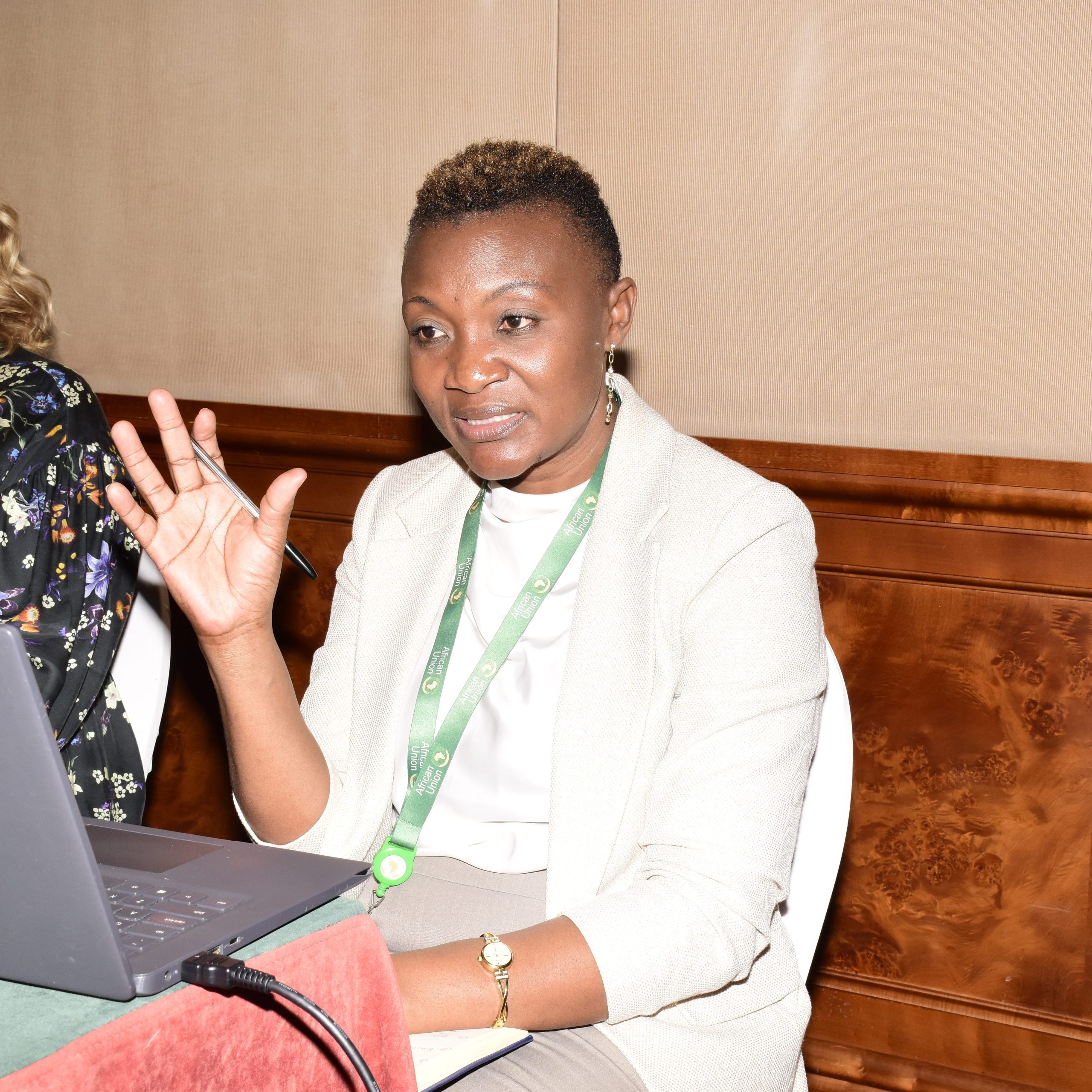 A woman in a room is sitting at a laptop and speaking