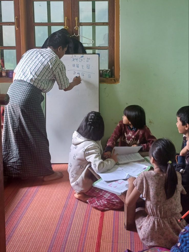 A teacher writes on a board in a classroom as children look on