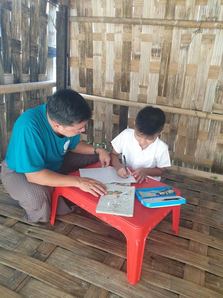 A father sits with his son at a desk helping him with his schoolwork