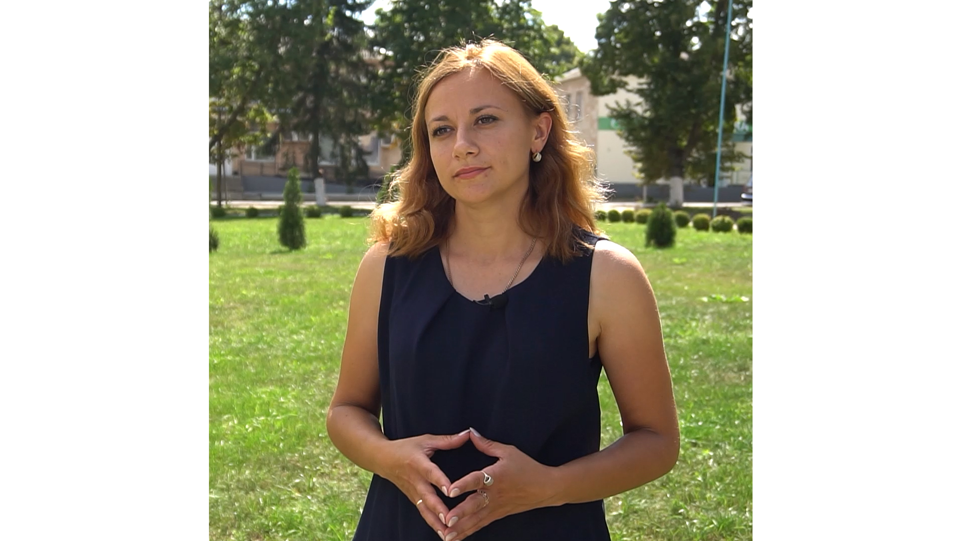 A woman stands outside and looks past the camera. She looks pensive and listening