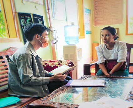 A man and a woman sit next to a table and talk. The man is wearing a mask.