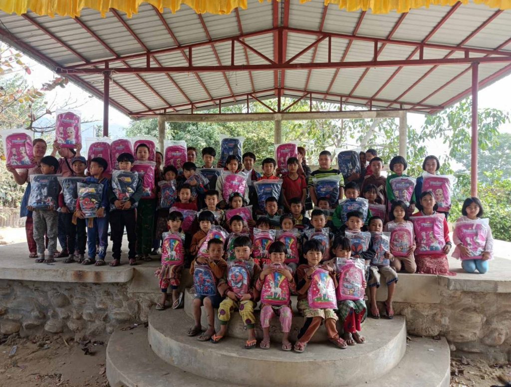 A class of young children pose underneath a shelter - they are all holding backpacks