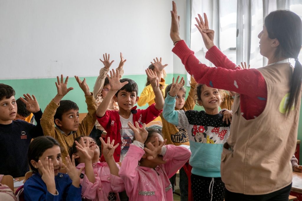 Opettaja näyttää lapsille sormilla numeroita ja lapset näyttävät omilla käsillään samaa määrää sormia Syyrialaisessa luokkahuoneessa.