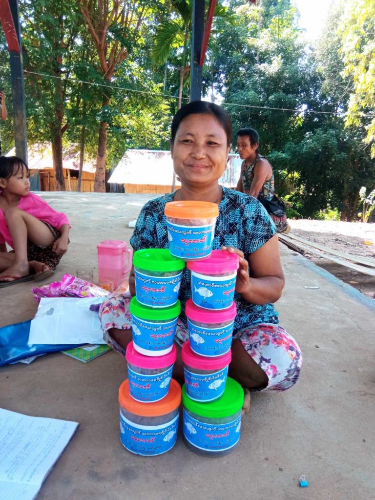 A smiling woman sits outside behind a pile of brightly coloured pots with a fish logo on them.