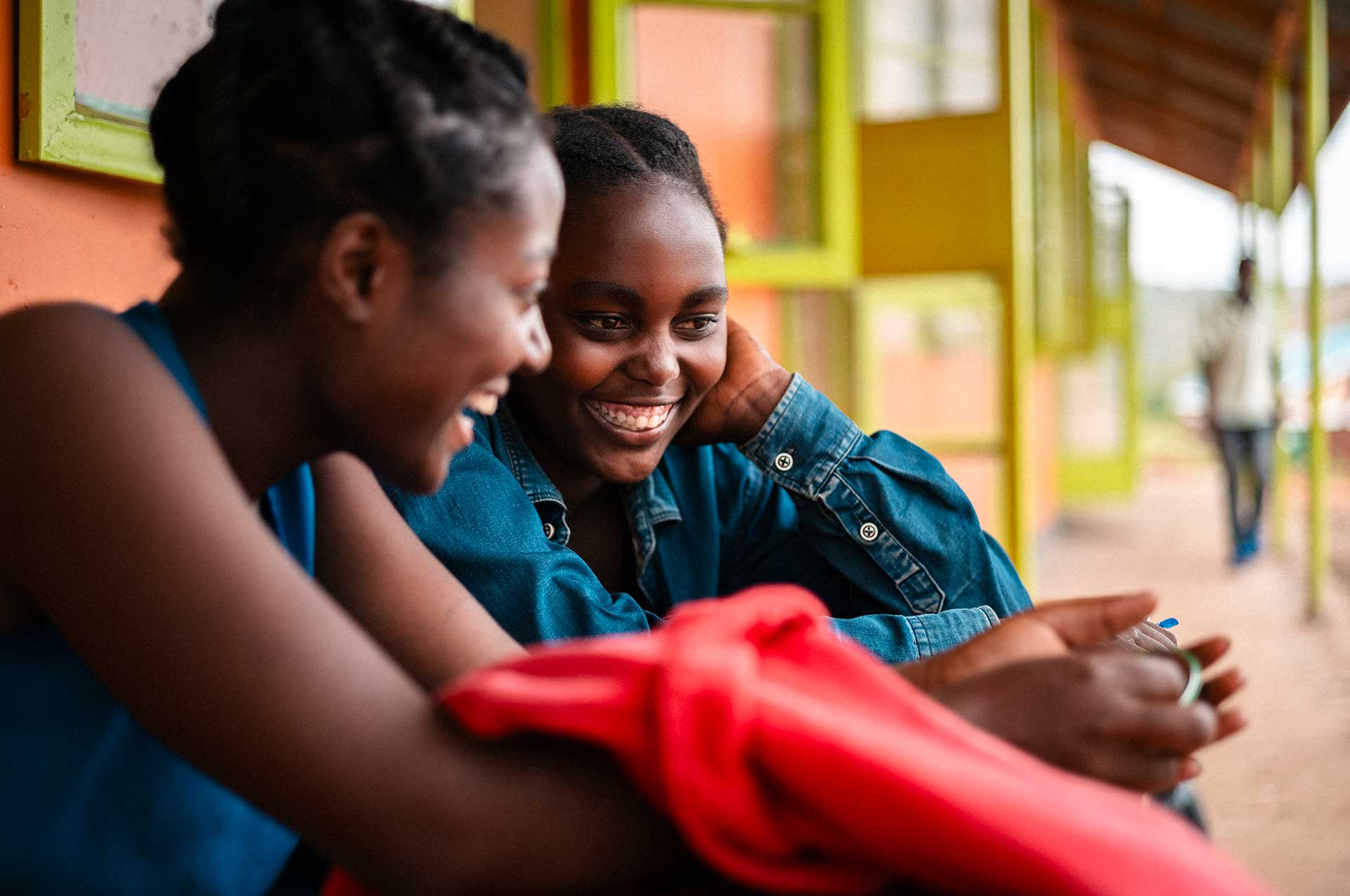 Kaksi kongolaista tyttöä nojaa koulurakennuksen seinään ja juttelee keskenään lähikuvassa.
