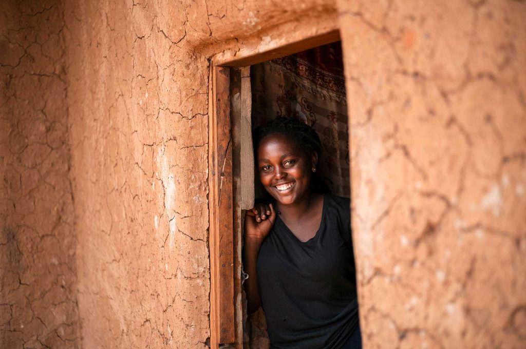 En ung kongolesisk kvinna tittar ut genom en dörröppning och ler.