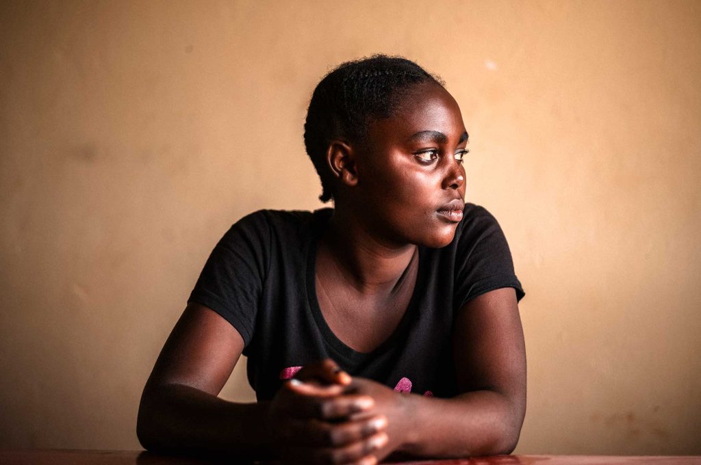 En ung kongolesisk kvinna sitter vid ett bord och tittar åt sidan.