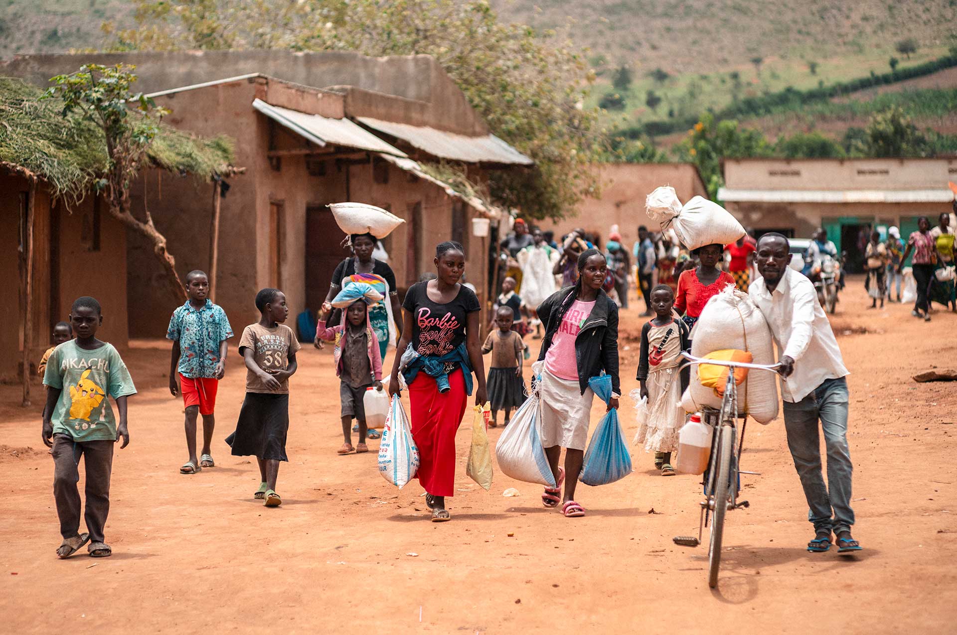 Ugandalaisen pakolaisasutusalueen tiellä kävelee paljon ihmisiä. Osaa taluttaa polkupyöriä ja monilla on käsissään ostospusseja.