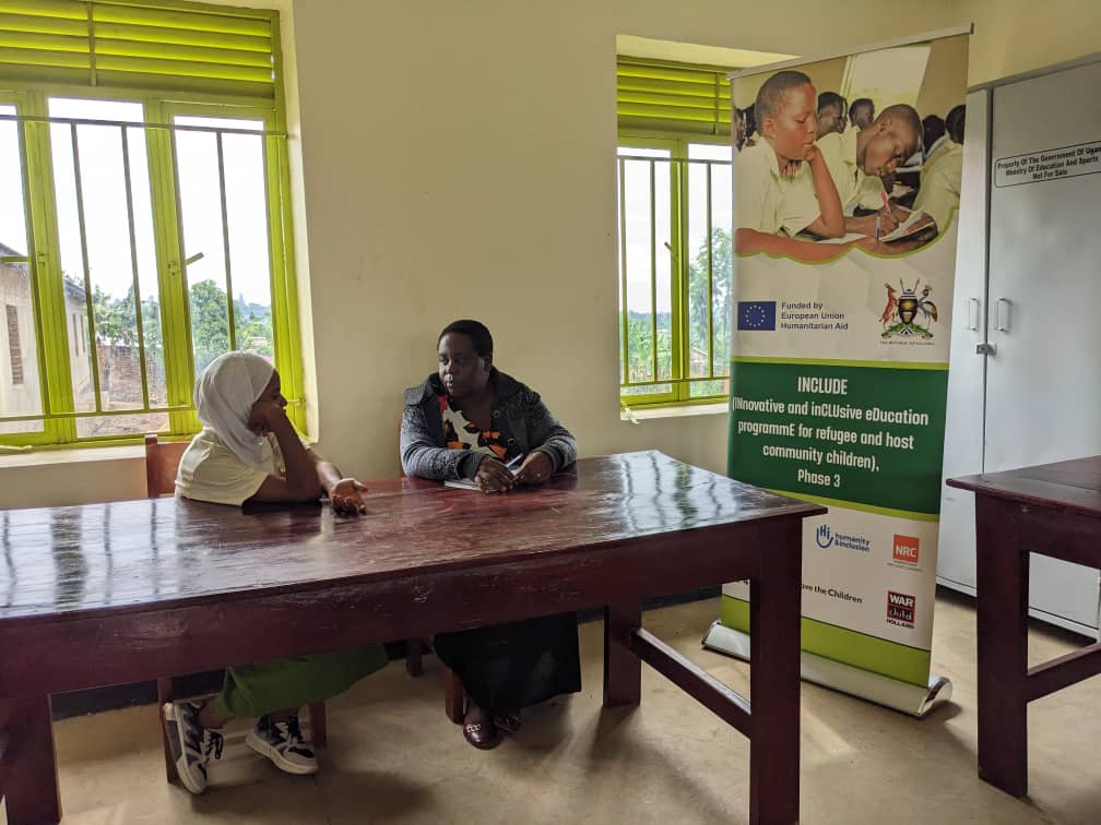 Two people are sitting at a large table in a room and having what looks like a serious conversation. An FCA banner with a EU logo stands to the side. 