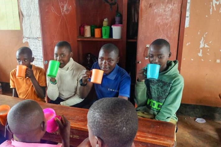 Students sit around a table in a classroom. They are all drinking from colourful mugs