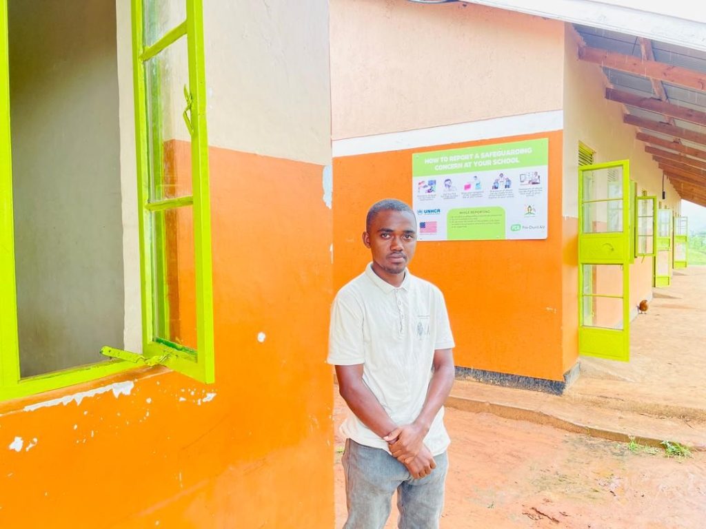 A man stands outside a school building. A poster in the background bears the FCA logo.