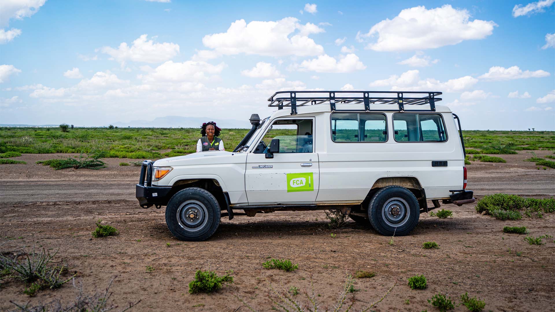 Land Cruiser standing in the plains of Kenya. A woman driver is standing next to the vehicle.