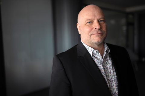 A man in a dark suit looks directly at the camera.