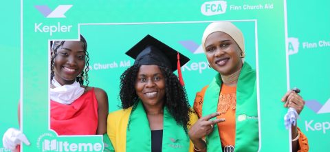 Three women pose holding a green frame around their faces. One is wearing a graduation cap.