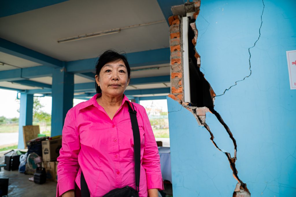 A woman in a bright pink shirt stands by a badly cracked wall.