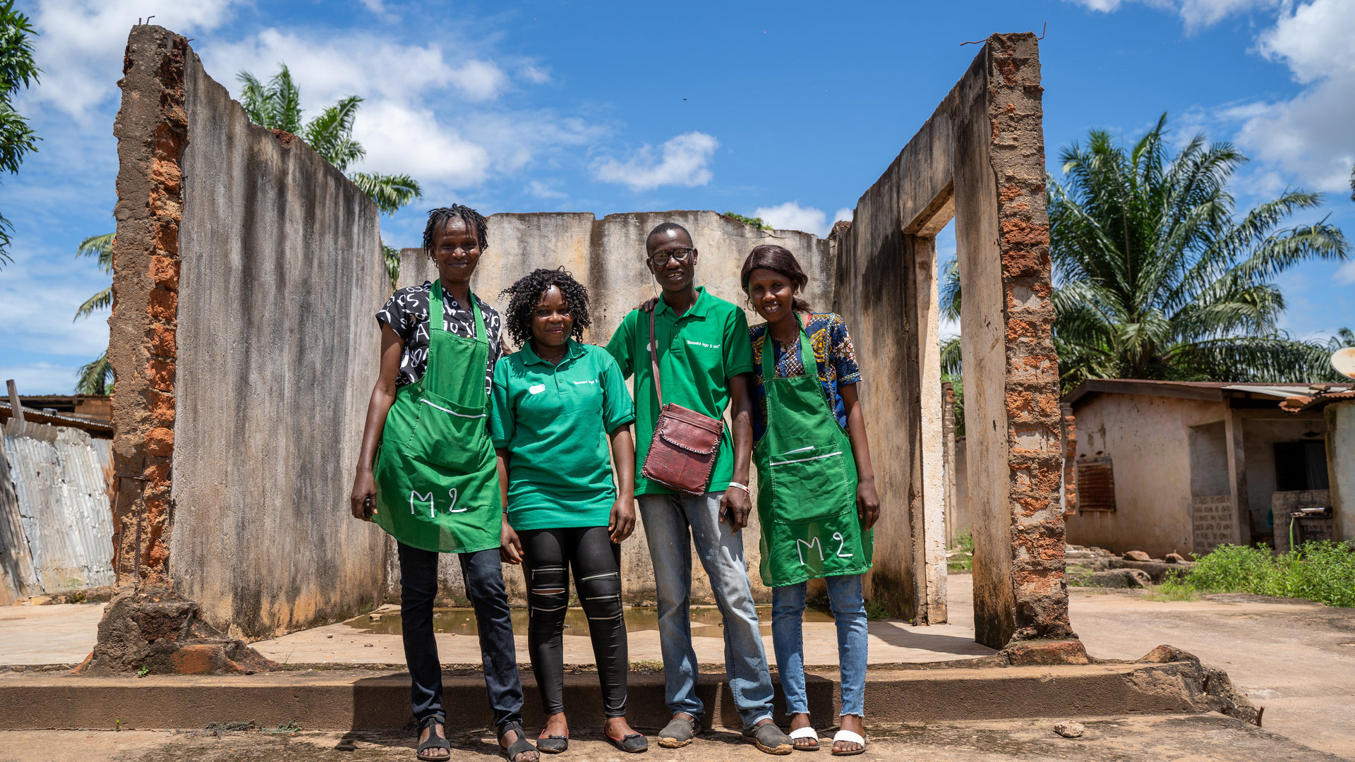 Four people in green aprons standing in front of a ruin.