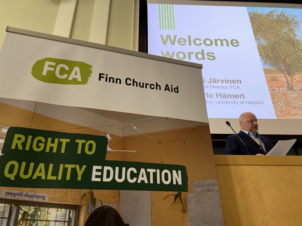 A man at a podium speaks. In the foreground there is a banner with the FCA logo and the slogan 'right to quality education'.