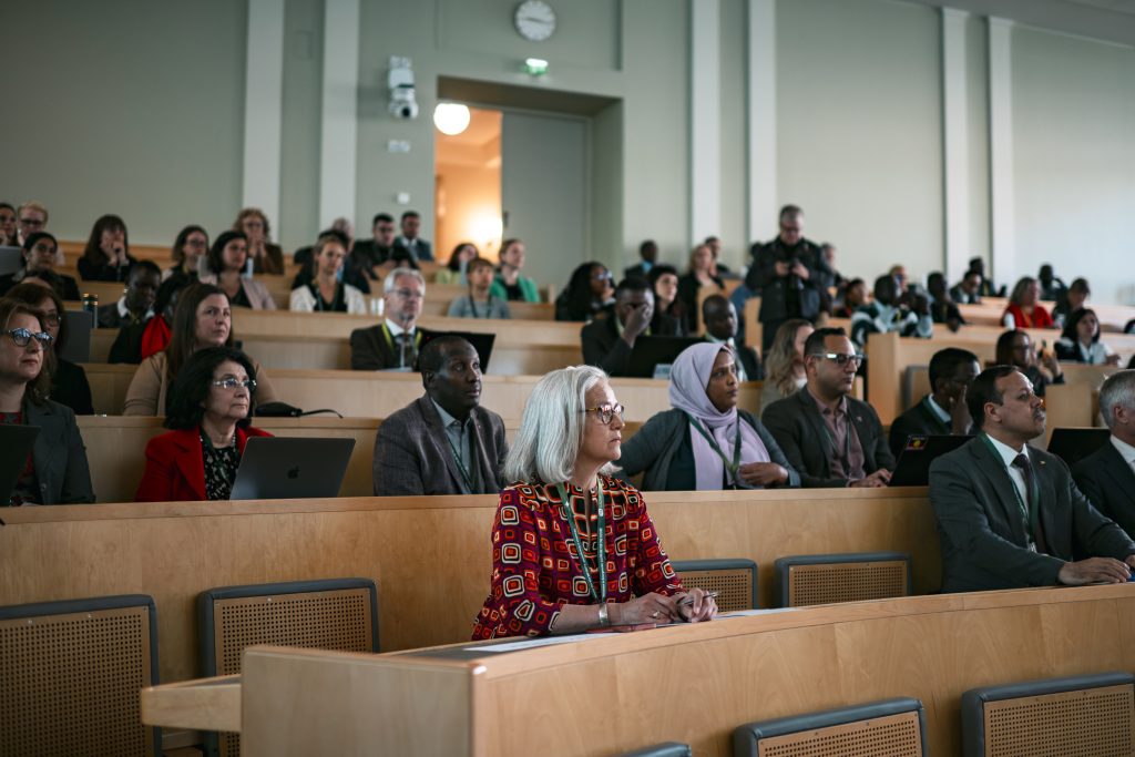 Several people listen attentively in a large auditorium