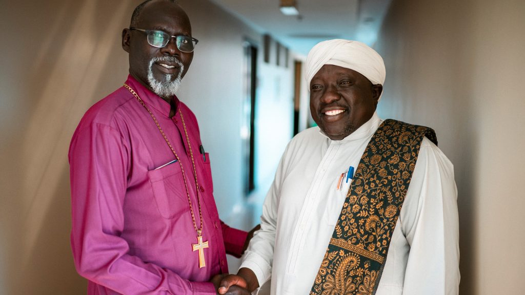 A man in bishop's clothing and one in traditional muslim garments shake hands.