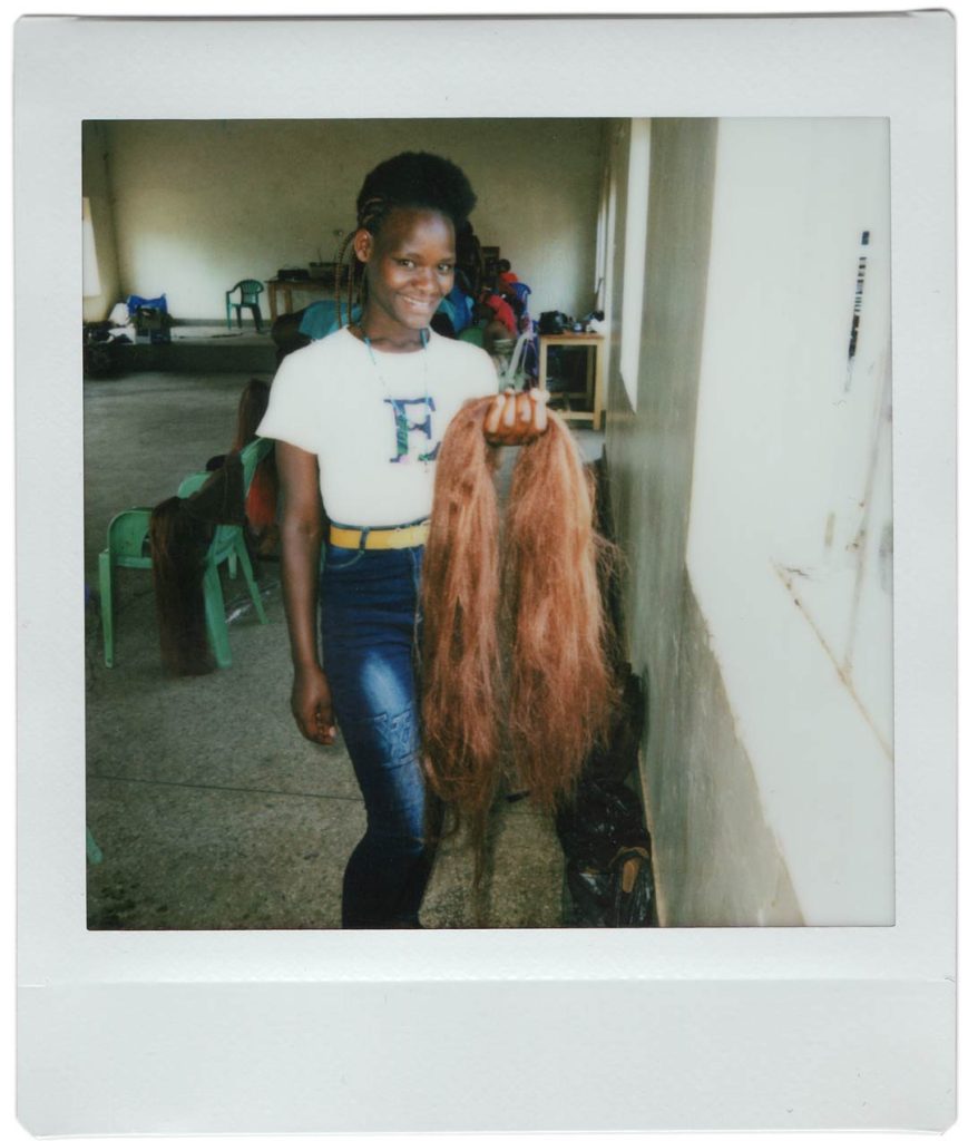A polaroid photo of a smiling woman holding a wig.