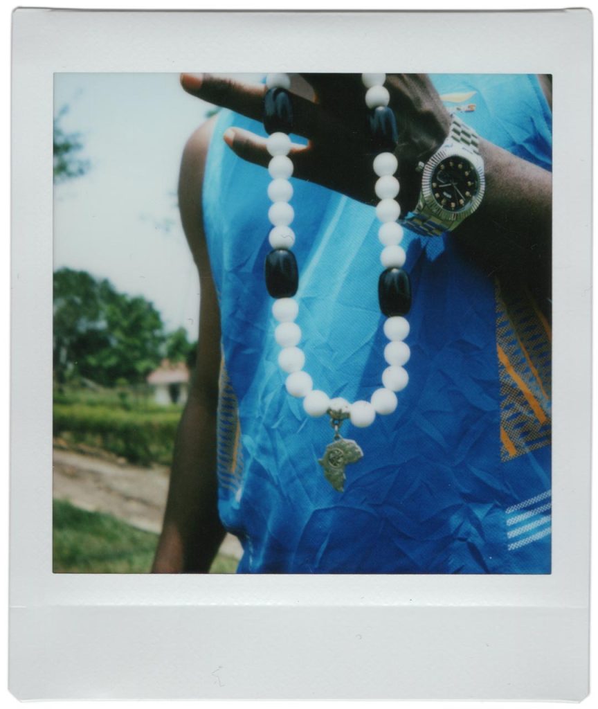A polaroid photo of a person in a blue shirt holding a chunky black and white bead necklace