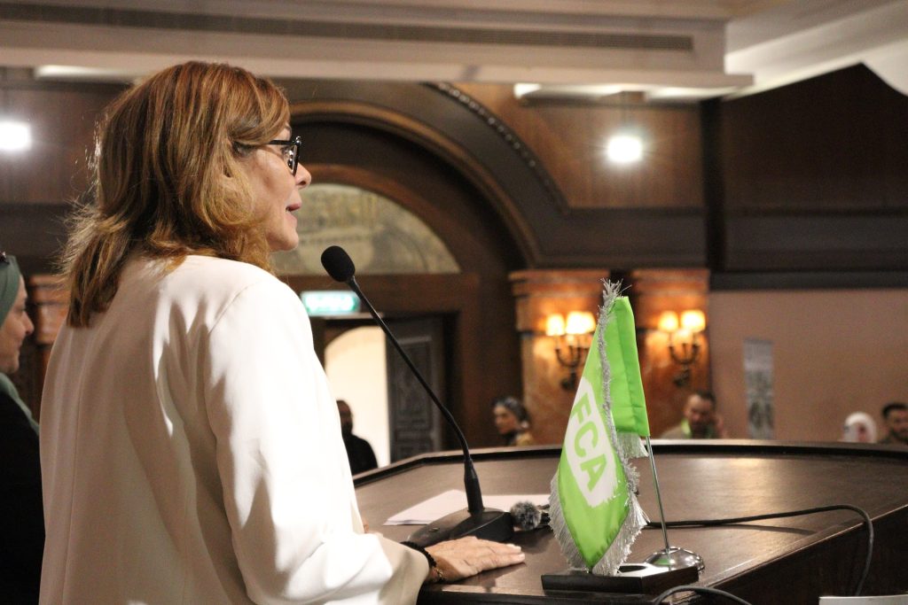 A woman speaking at a podium featuring the FCA flag