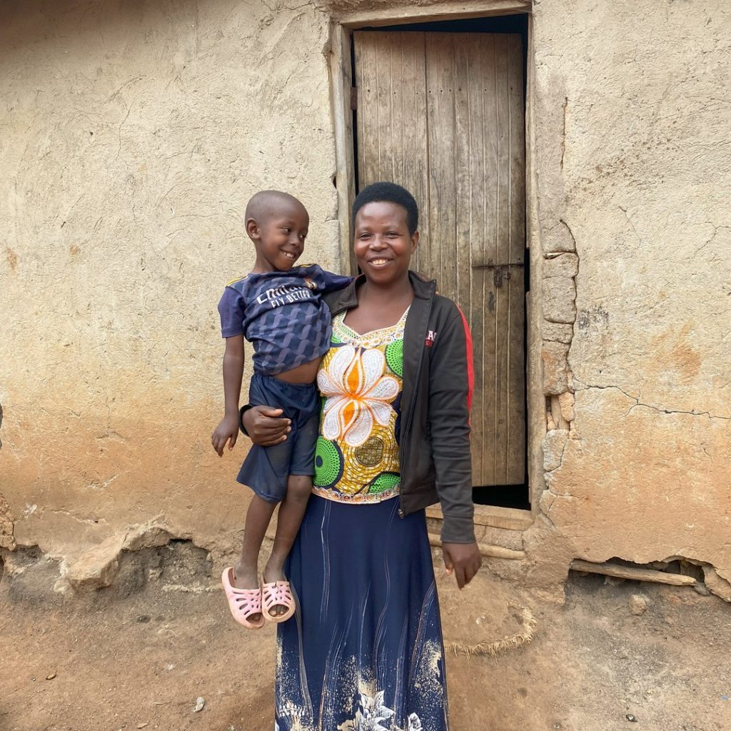 A woman standing in front of the doorway to a house, carrying a young boy in her arms.