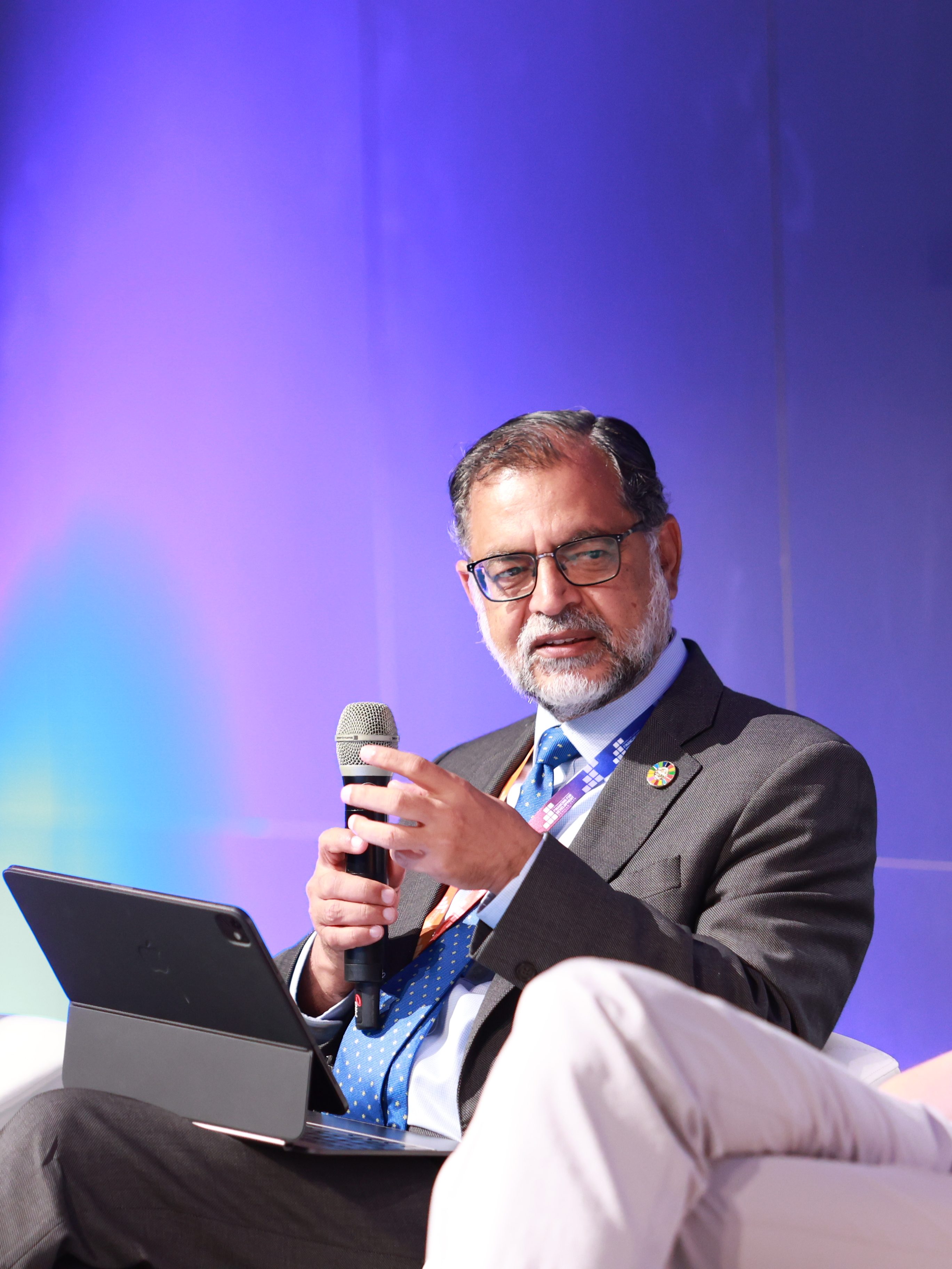 A seated man with a microphone speaks, while a woman and a man either side listen.