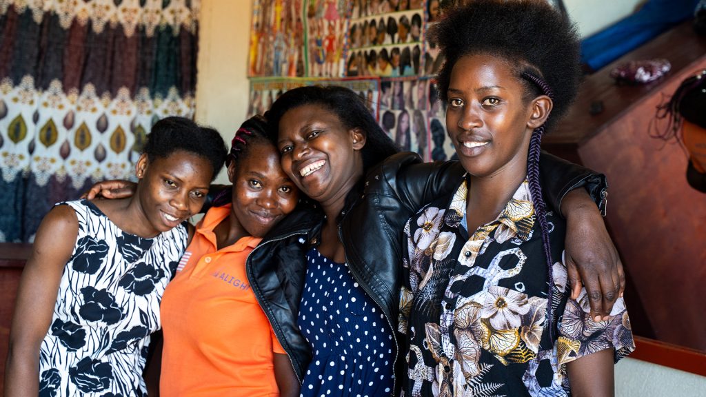 Four women standing with their arms around each other in a salon. 