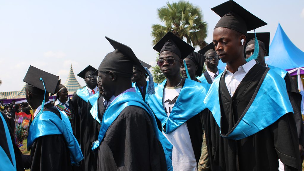 Teacher graduates standing in black robes, hats and blue scarves