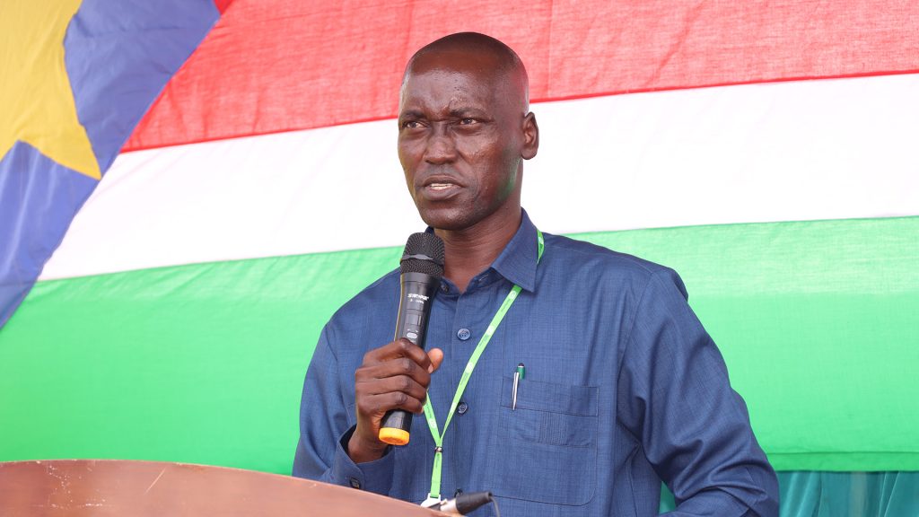 A man talking in a microphone in front of a South Sudanese flag