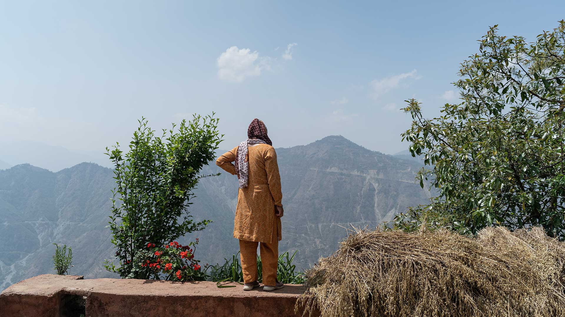 Nepalilainen nainen seisoo ulkona maaseudulla selin kameraan. Nainen katselee kaukaisuuteen, missä näkyy vuoria.