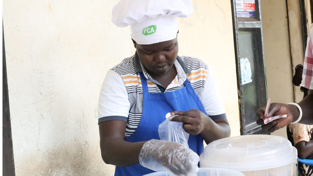 A woman standing in a stall, selling baked goods. Someone is handing her money.